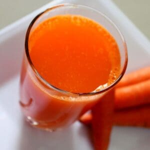 serving carrot juice in a glass with some carrots on a plate