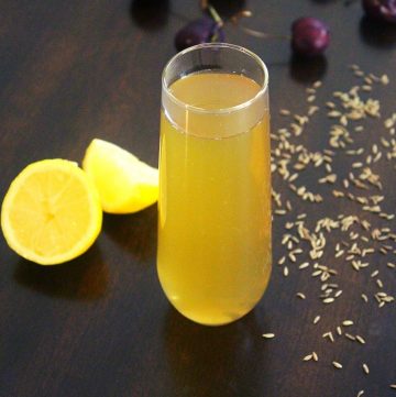 cumin water served in a tall thin glass with lemon slices and cumin seeds spread around