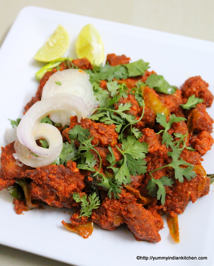 hyderabadi chicken 65 on a plate with onion rings and lemon wedges