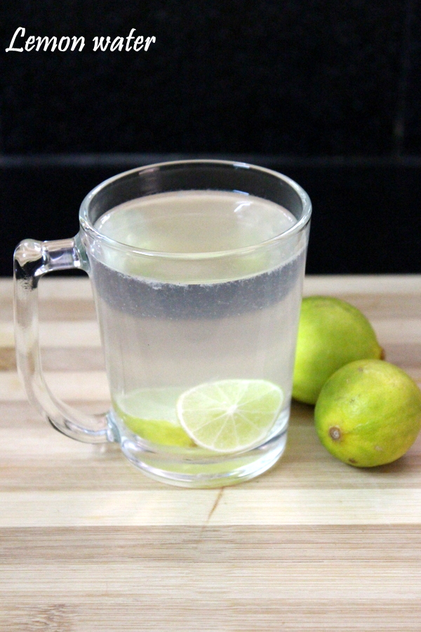 lemon water inside the glass with leon slices in it and two lemons beside 