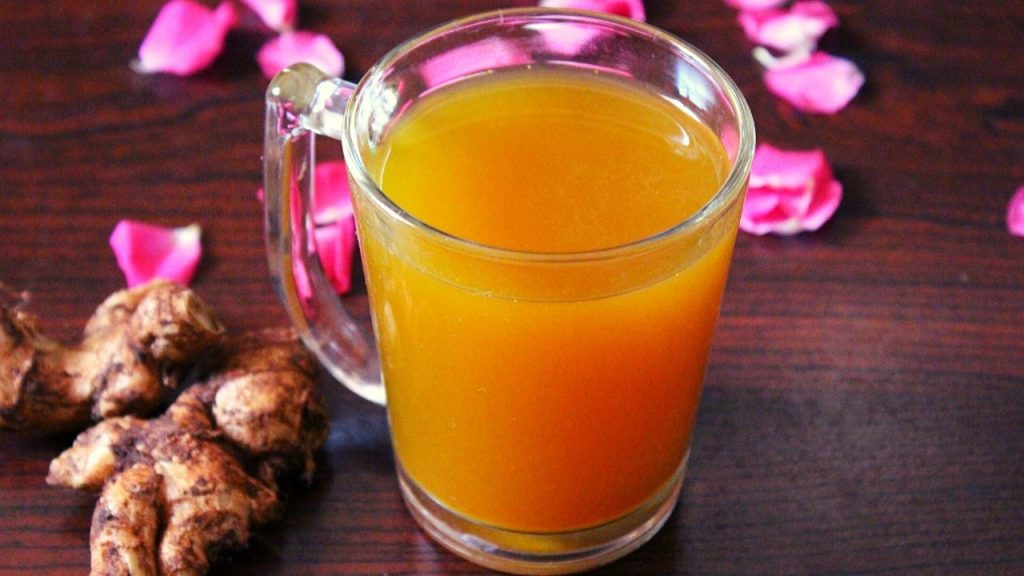 turmeric tea in a glass with rose petals  spread around and ginger piece beside