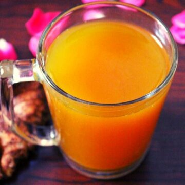 turmeric tea in a glass with rose petals spread around