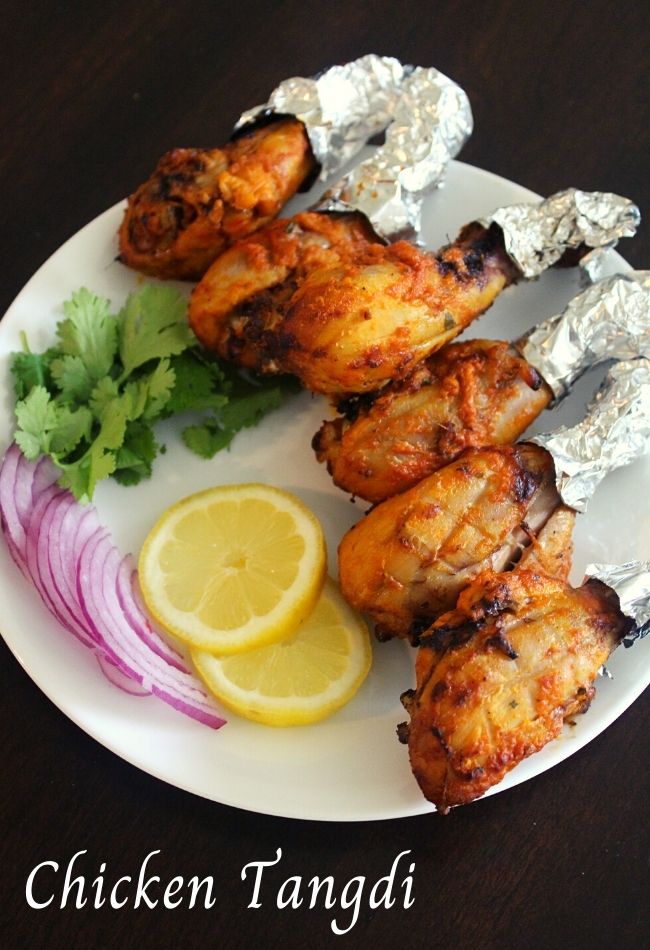 Chicken legs or tangdi kabab on a plate with lemon slices and onions