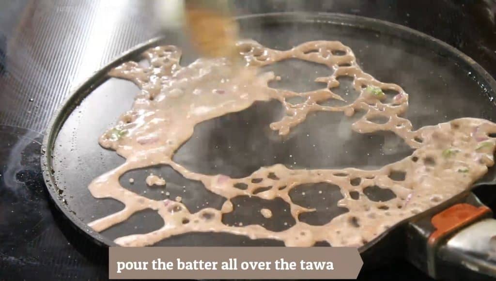 Taking a ladle full of thin batter and covering the tawa