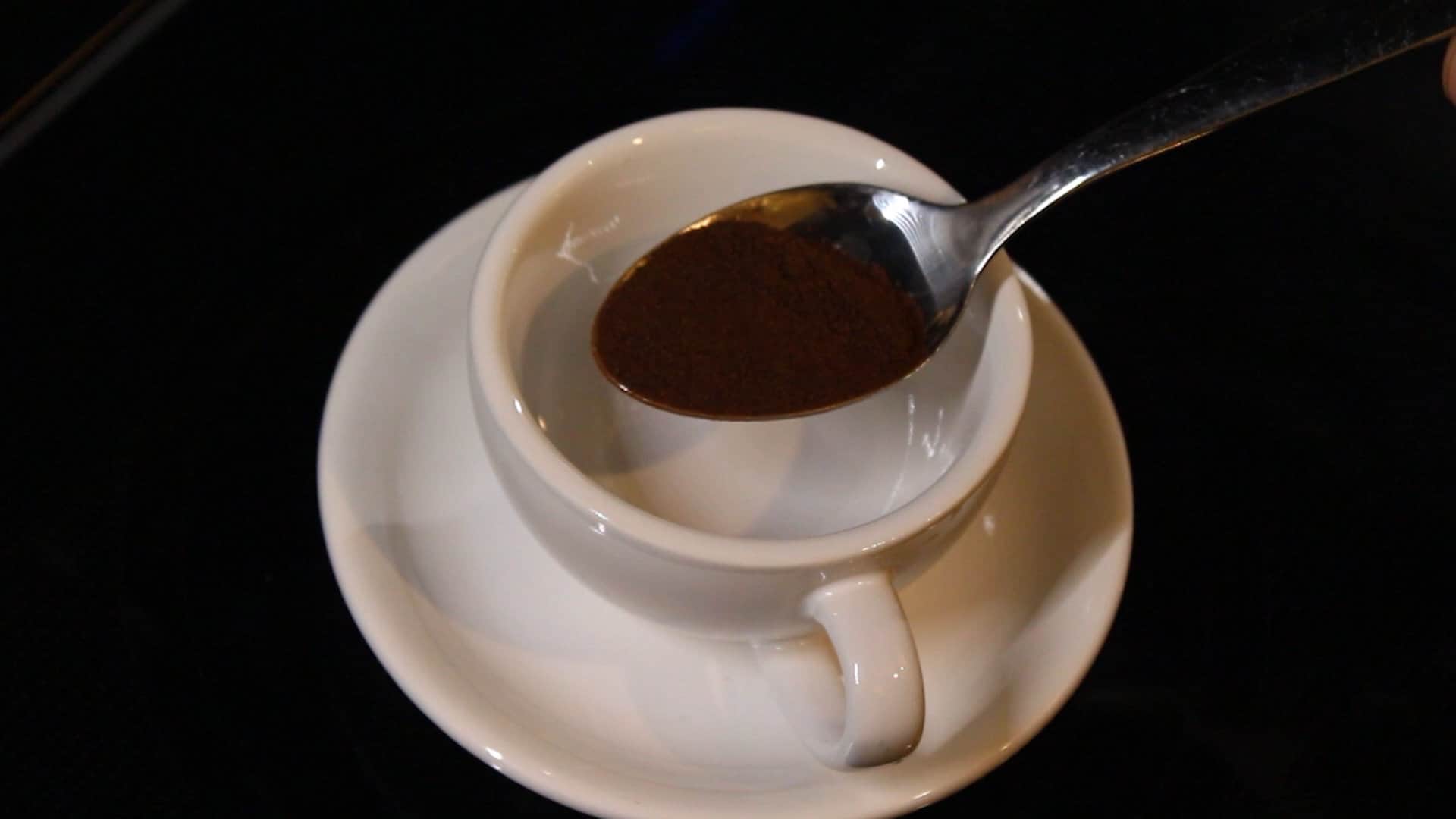 adding coffee powder in a plain white cup