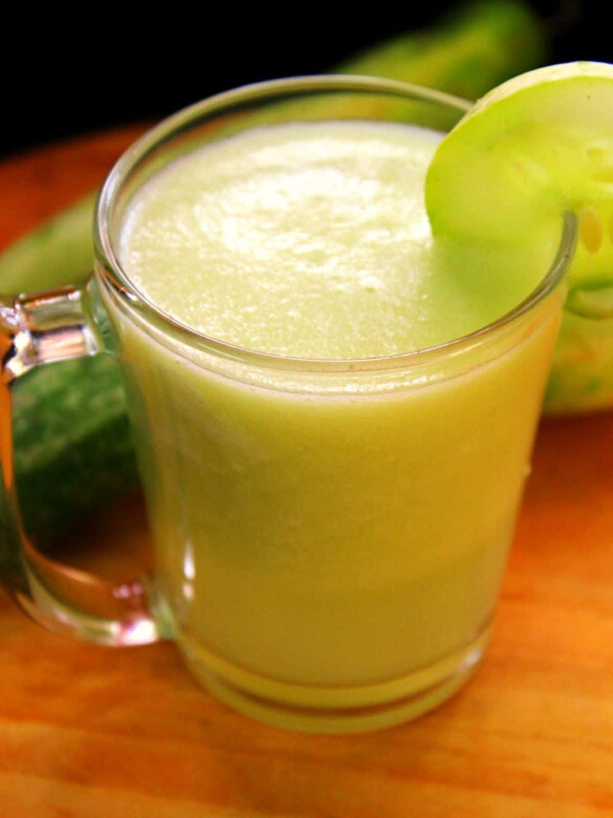 cucumber juice in a glass with a cucumber slice to the glass