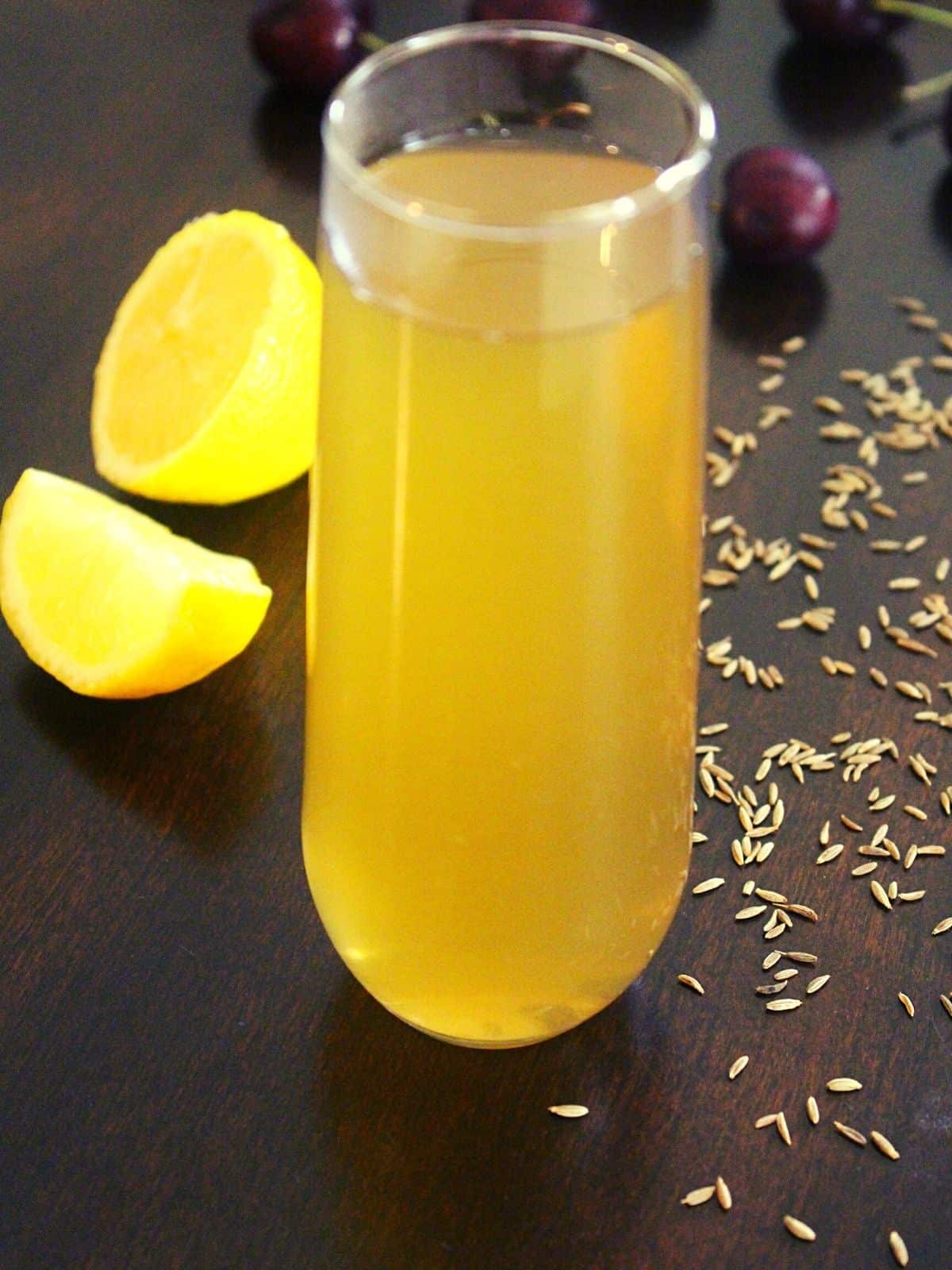 cumin water in a tall thin glass with lemon and cumin seeds spread around