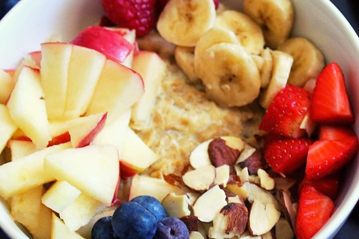 cooked rolled oats in a bowl topped with chopped banana, apples, almonds, berries