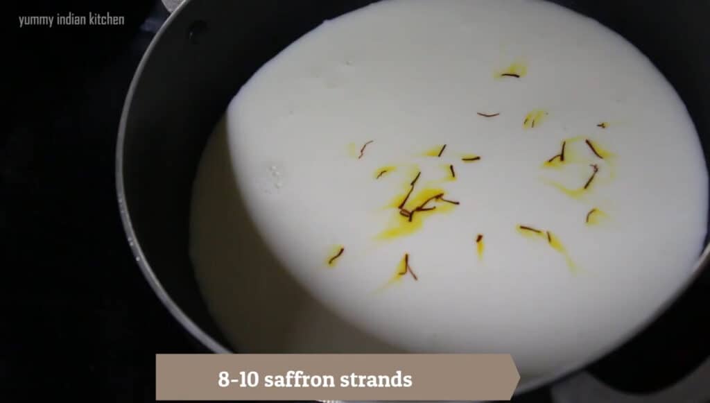 Adding full cream milk to a pan and adding saffron strands into it