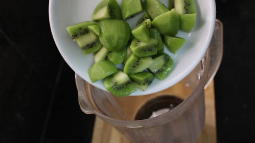 Adding the slices of the kiwi into a juice blender