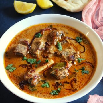 lamb pasanda in a bowl with lemon wedges and naan beside