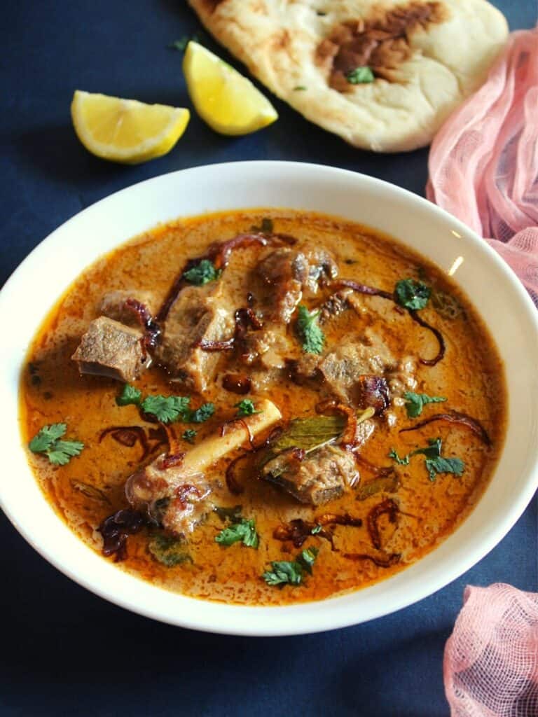 lamb pasanda in a bowl with lemon wedges and naan beside