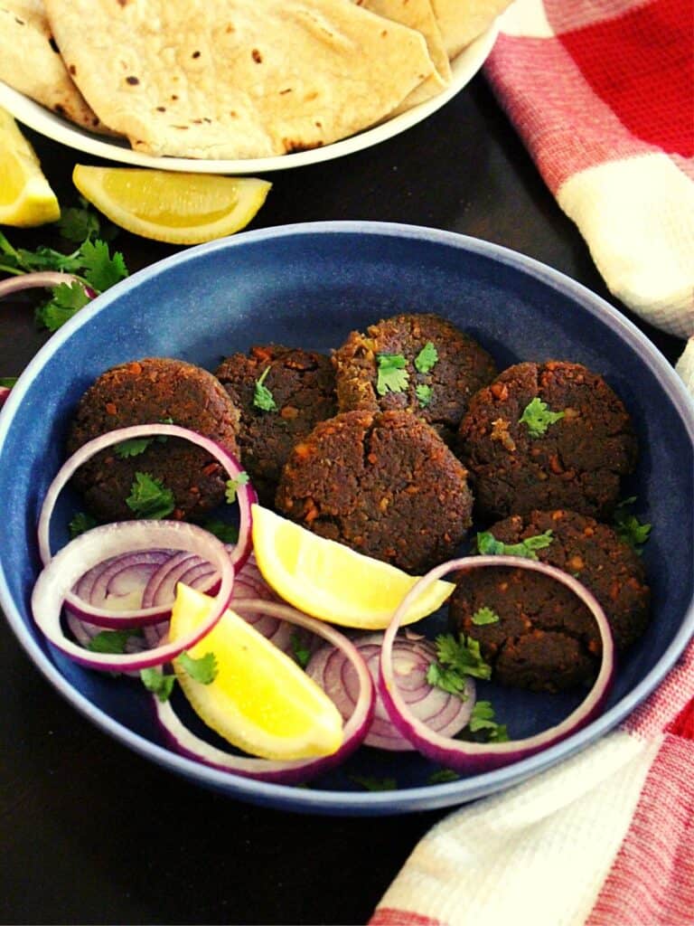shami kabab in a bowl with onion rings and lemon