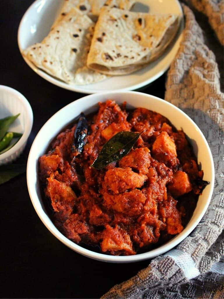 achari chicken served in a bowl with chapati beside
