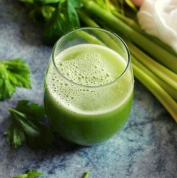 celery juice served in glass with celery stalks beside