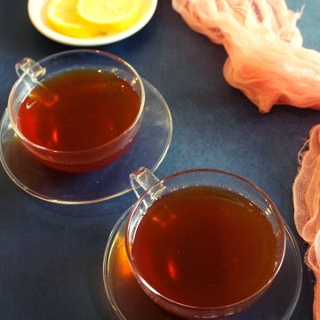 black tea in two cups with lemon slices placed beside