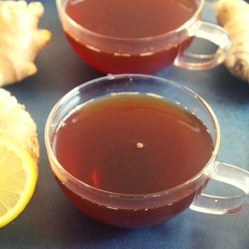 lemon tea in two cups for treating cold and weight loss with ginger pieces beside