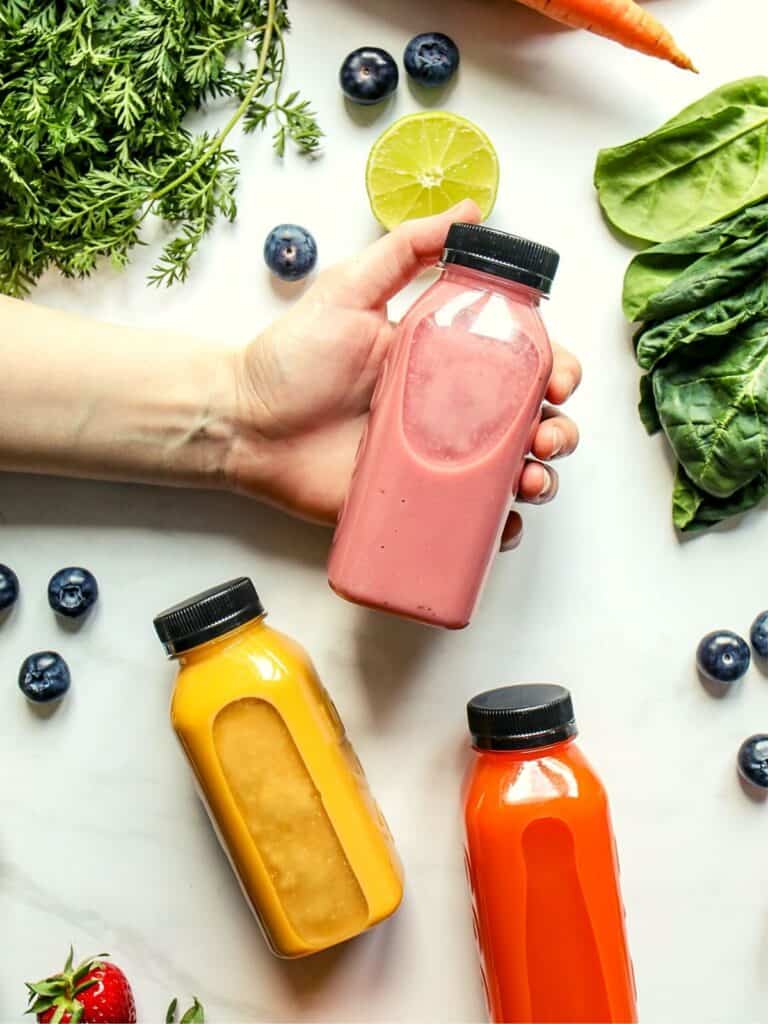 detox smoothies in smoothie bottles for weight loss diet with berries, kale, spinach, carrots showing around