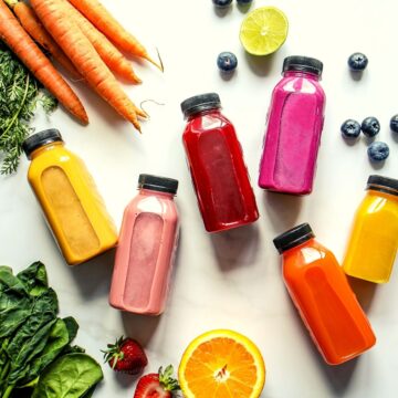 different smoothies in different smoothie bottles with carrots. kale, ginger, berries around