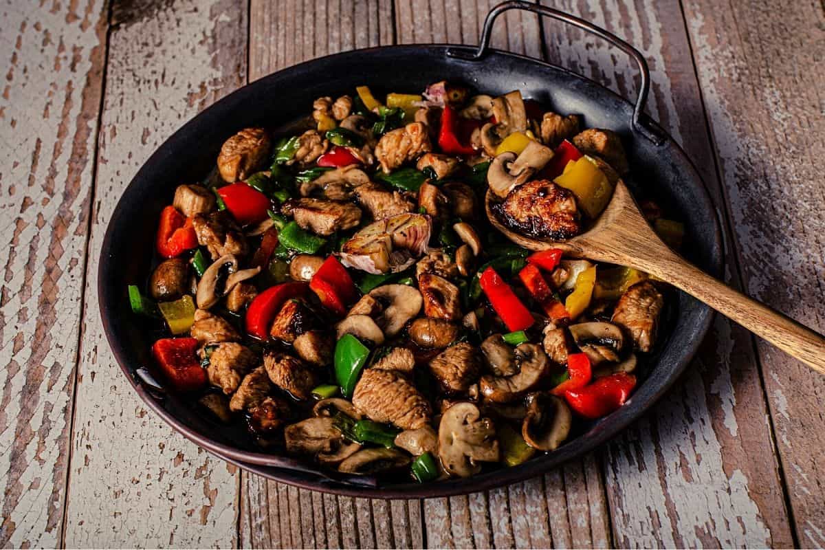 chicken and veggies stir fry in a wok with a spatula