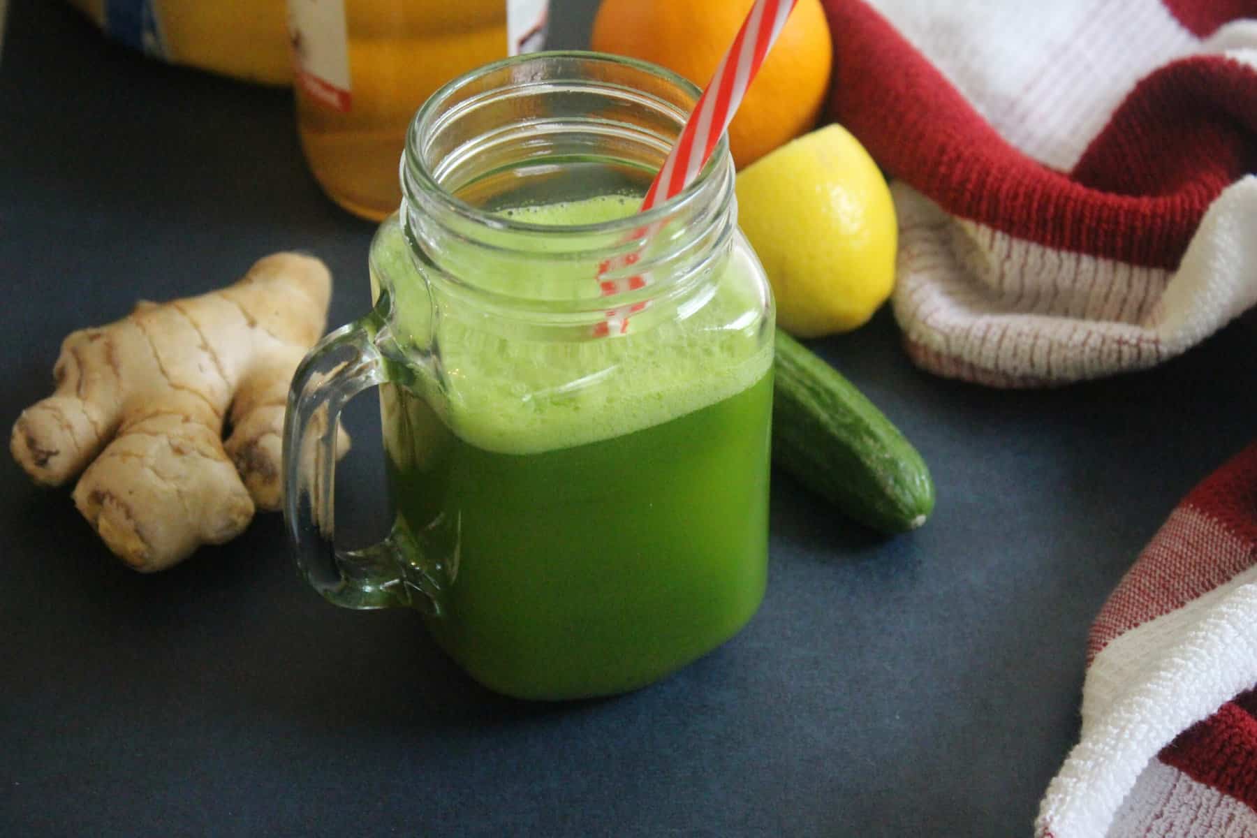 green color smoothie in a mason jar with ginger, lemon, apple cider around