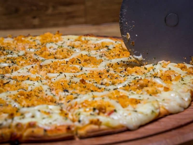 optavia chicken pizza with cheese and chicken shown with a pizza cutter cutting the pizza