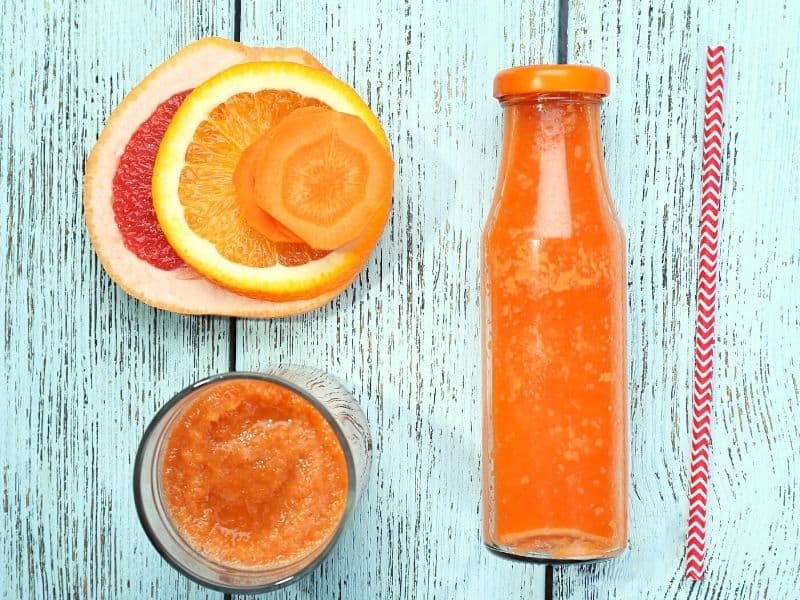 orange detox smoothie in a  bottle with oranges beside as a detox smoothie for weight loss