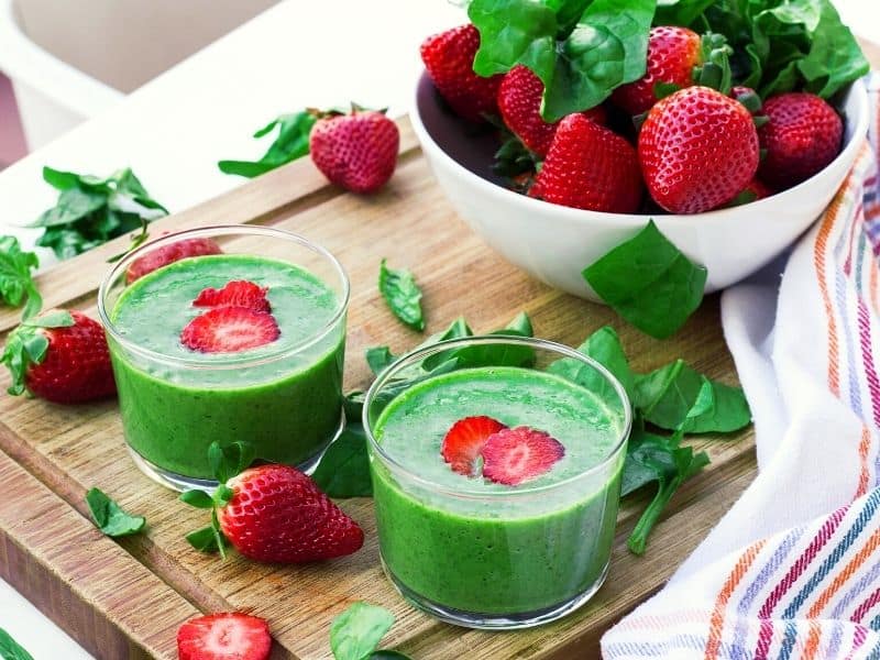 strawberry and spinach in a glass with strawberries placed in a bowl and spinach around