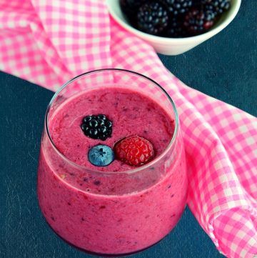 berry smoothie with yogurt in a glass with berries in a round bowl