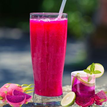 dragon fruit tea refresher in a tall glass with red and purple dragon fruit beside the glass
