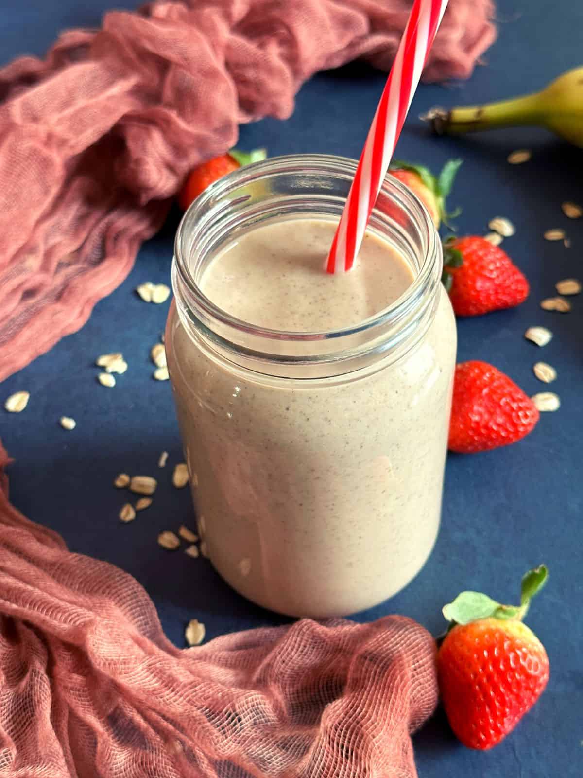 1000 calorie smoothie for weight gain in a mason jar with strawberries thrown around the jar