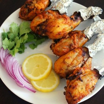 tangdi kabab made using chicken legs on a plate with onions and lemon wedges